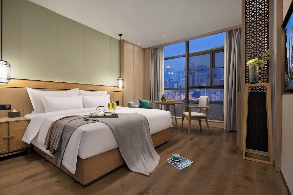 Habitación de hotel con una cama grande, un escritorio y vistas a la ciudad.