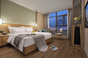 Habitación de hotel con una cama grande, un escritorio y vistas a la ciudad.