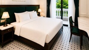 A hotel room with a bed, nightstands, a chair, a table, and a view of greenery through the window.