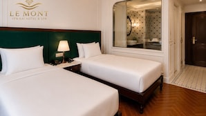 Quarto de hotel com duas camas, uma mesa de cabeceira com abajur, um espelho grande e piso de madeira.
