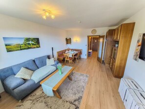 Ein Wohnzimmer mit einer Couch, einem Couchtisch, einem Esstisch mit Stühlen und einer Küchenzeile mit Holzschränken.