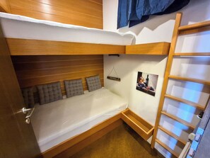 Ein Schlafraum mit Etagenbetten, einem Holz-Kopfende, einem kleinen Nachttisch und einem an der Wand befestigten Regal.