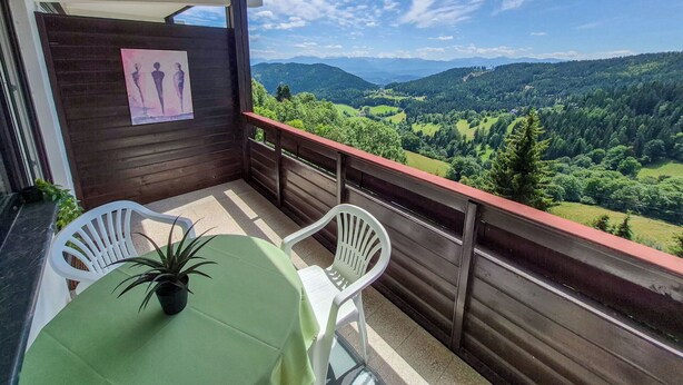 Un balcone con tavolo e sedie, affacciato su un paesaggio montuoso.