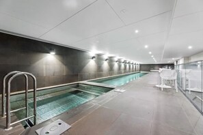 A modern indoor swimming pool with a long, narrow design, surrounded by a tiled floor and walls, and equipped with metal handrails. - 2BR Inner Brunswick with City Views (Brunswick East)