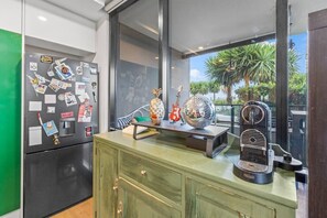A kitchen with a refrigerator, a coffee maker, and a window with a view of palm trees. - 2BR Inner Brunswick with City Views (Brunswick East)