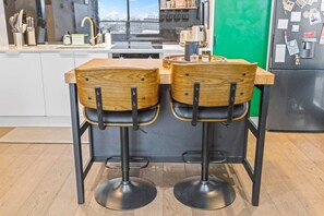 A modern kitchen with two wooden bar stools, a stainless steel refrigerator, and a green wall. - 2BR Inner Brunswick with City Views (Brunswick East)