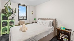 Et soveværelse med en seng, et vindue, et grønt skab med audio udstyr og en plante.