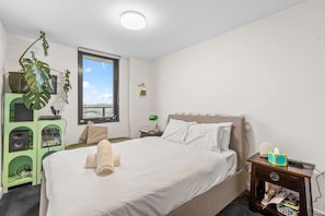A bedroom with a bed, a window, a green cabinet with audio equipment, and a plant. - 2BR Inner Brunswick with City Views (Brunswick East)