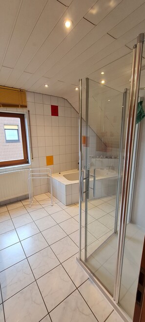 A modern bathroom with a glass shower enclosure, a bathtub, and a window.