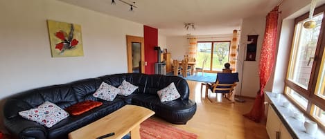 Un salon avec un canapé en cuir noir, une table basse en bois et un coin repas comprenant des chaises et une table en bois.