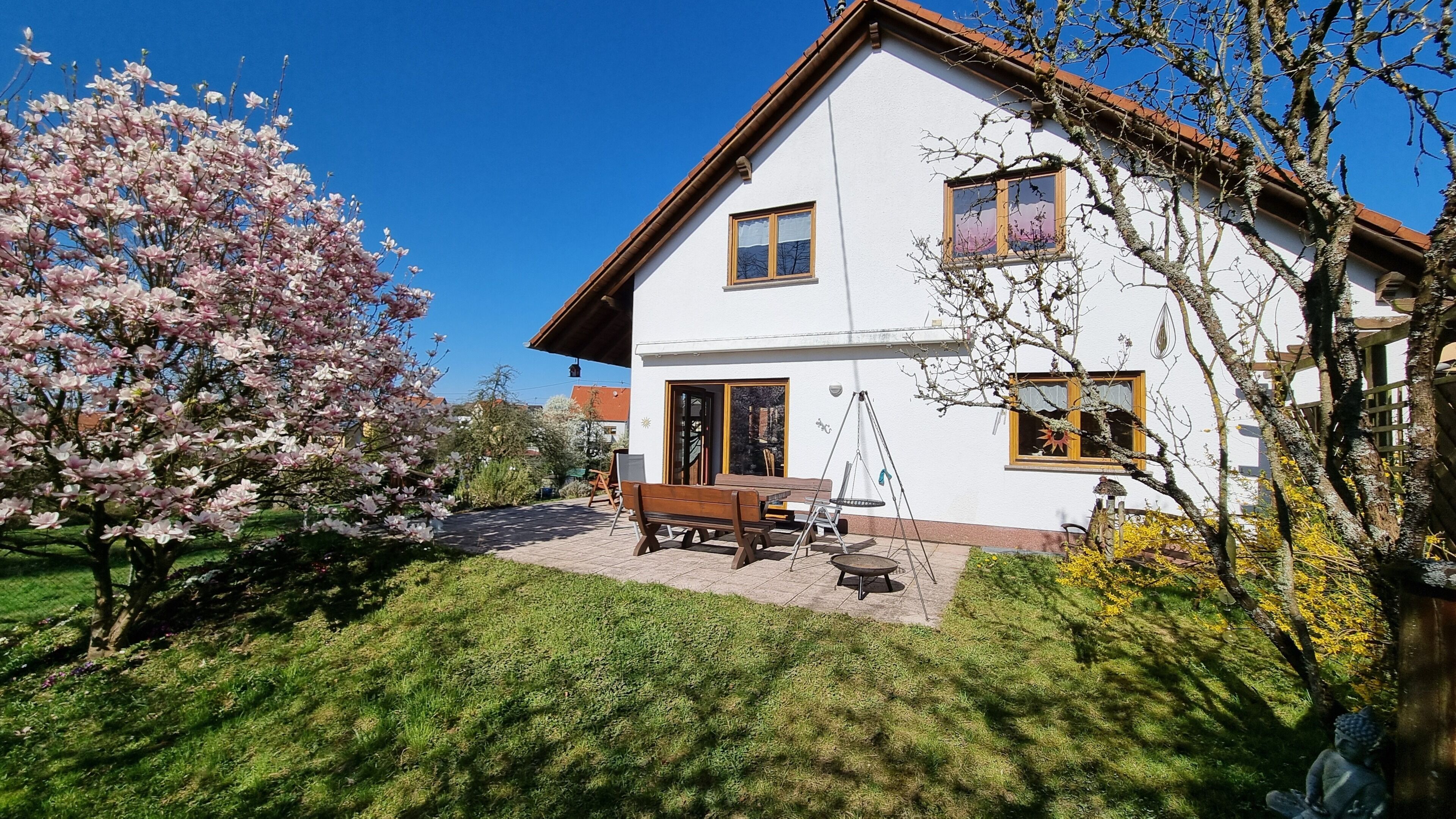 Een tweelaags huis met een terras, een schommel en een tuin met bloeiende bomen.