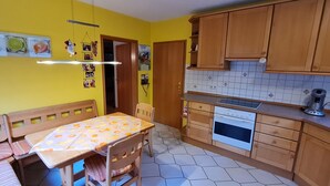 Una cocina compacta con armarios de madera, una mesa de comedor con mantel estampado de frutas y piso de baldosas.