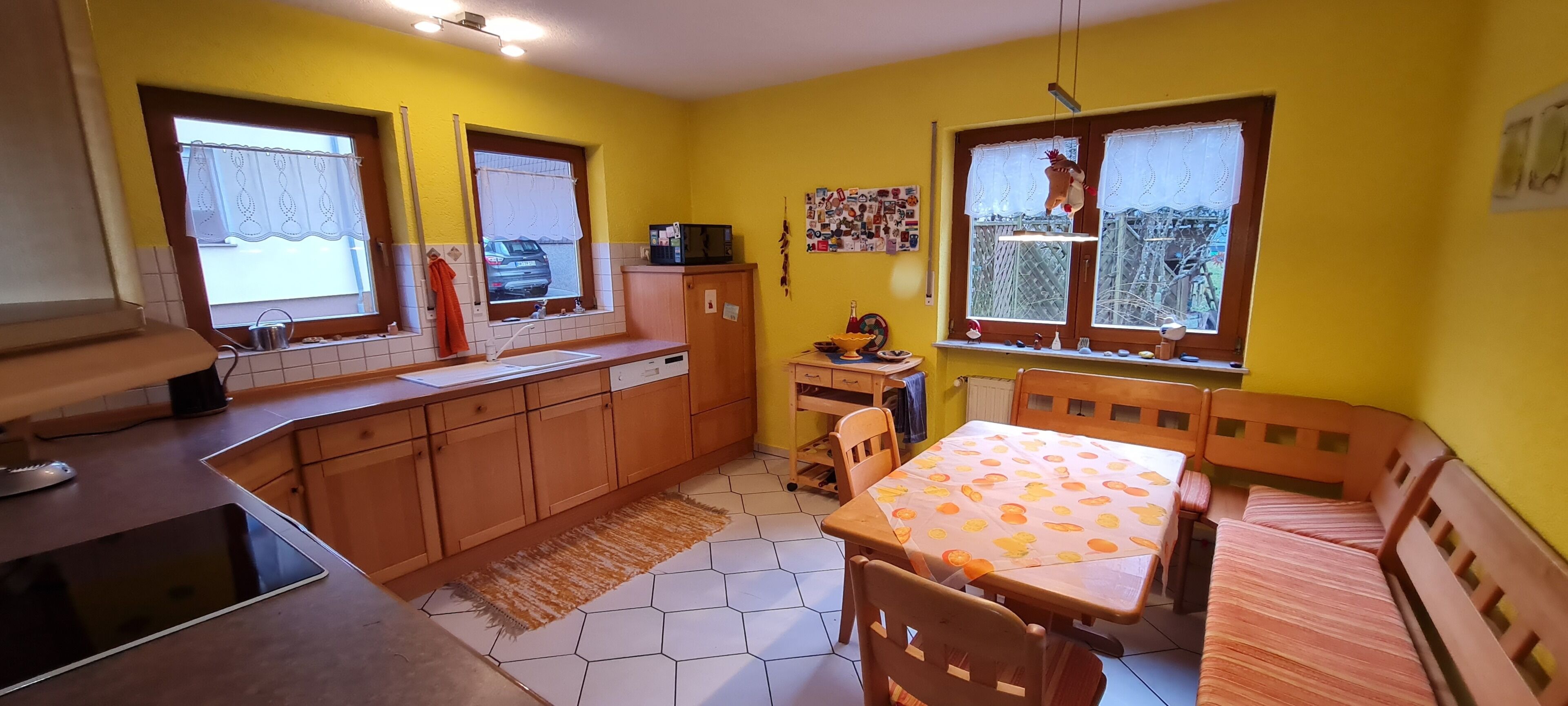 A kitchen with wooden cabinets, a dining table with a patterned tablecloth, and a window with a view of trees.