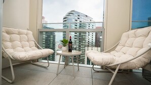 Ein Balkon mit zwei Polsterstühlen, einem kleinen Tisch, einer Weinflasche und einem Blumentopf.