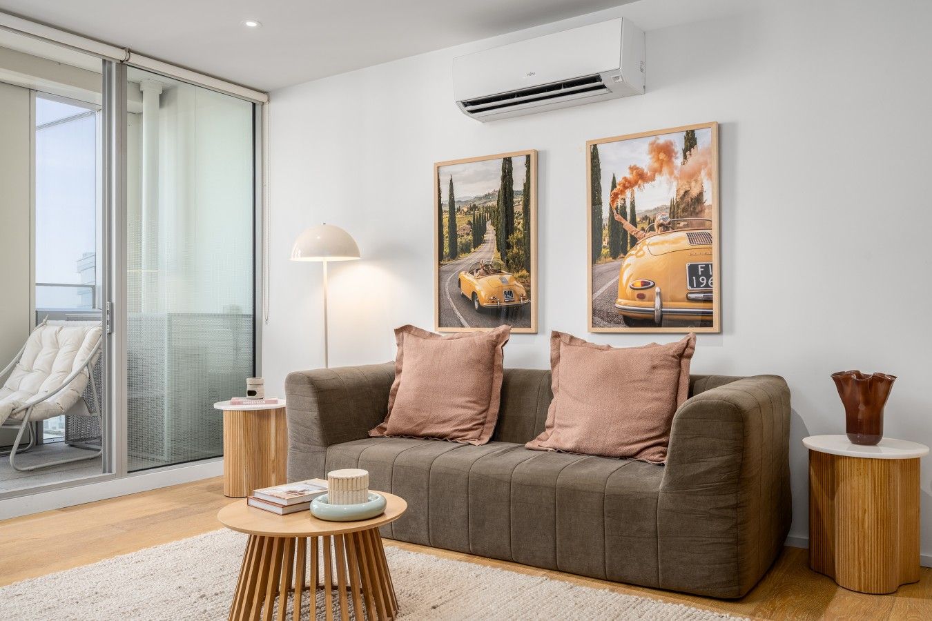 A modern living room with a grey sofa, two cushions, a round coffee table with books, a floor lamp, and two framed pictures on the wall.