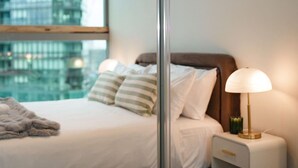 Ein Hotelzimmer mit Bett, Nachttischlampe und Blick auf eine Stadtlandschaft durch ein Fenster.