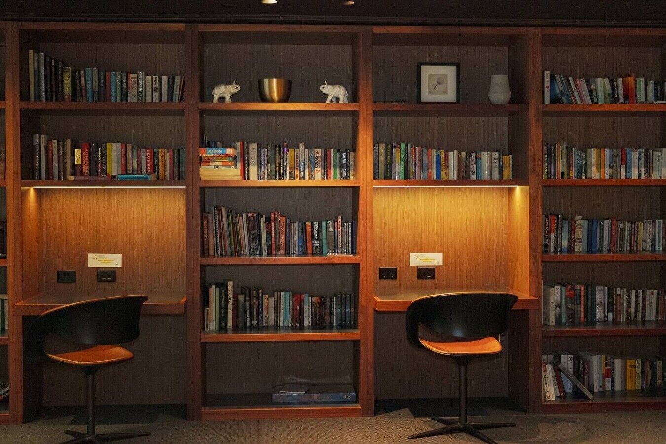 Una biblioteca con numerose scaffalature, due poltrone nere e alcuni elementi decorativi.