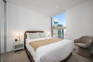 Ein modernes Schlafzimmer mit einem großen Bett, Nachttischlampen, Blick auf eine Stadtlandschaft und einem Fenster.