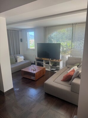 Ein modernes Wohnzimmer mit einem Flachbildfernseher, zwei Sofas, einem Couchtisch und einem Fenster mit Jalousien.