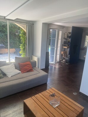 Uma sala de estar moderna com um sofá cinzento, uma mesa de centro de madeira e vista através de grandes janelas.