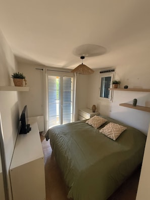 Ein Schlafzimmer mit einem Bett, einem Schminktisch, einem Fernseher, einem Deckenventilator und einem Fenster mit Vorhängen.