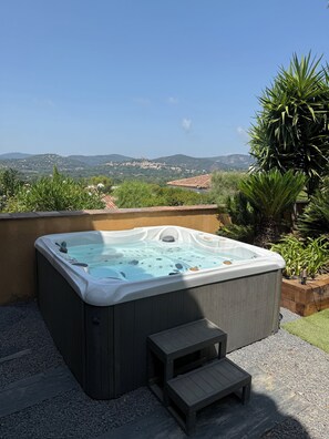 Uma banheira de hidromassagem com um banco de madeira em um jardim, com vista para uma cidade e colinas ao longe.