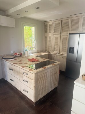 A modern kitchen with a central island, built-in cabinets, and a stainless steel refrigerator. - House with a View of the Castle • Jacuzzi • Fire pit • Fitness Area • Beaches 10 minutes away (Cogolin)