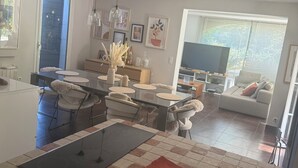 Eine moderne Küche mit Kochinsel, Essbereich mit Stühlen und Wohnzimmer mit Sofa und Fernseher.