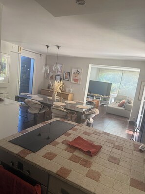 Eine moderne Küche mit Kochinsel, Essbereich mit Stühlen und Wohnzimmer mit Sofa und Fernseher.