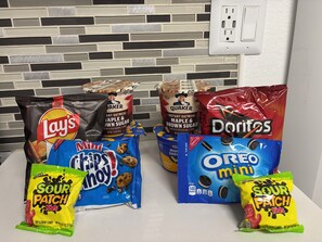 Verschiedene Snacks, darunter Lay's Chips, Quaker Haferflocken, Doritos, Mini Krispy Kreme Donuts und Sour Patch Kids.