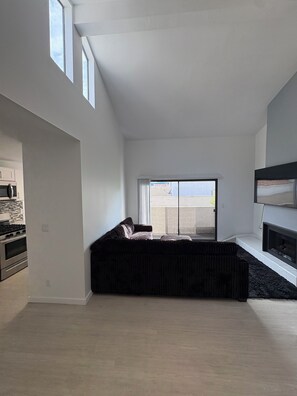 Ein modernes Wohnzimmer mit einem dunklen Sofa, einem Kamin und einem großen Fenster.