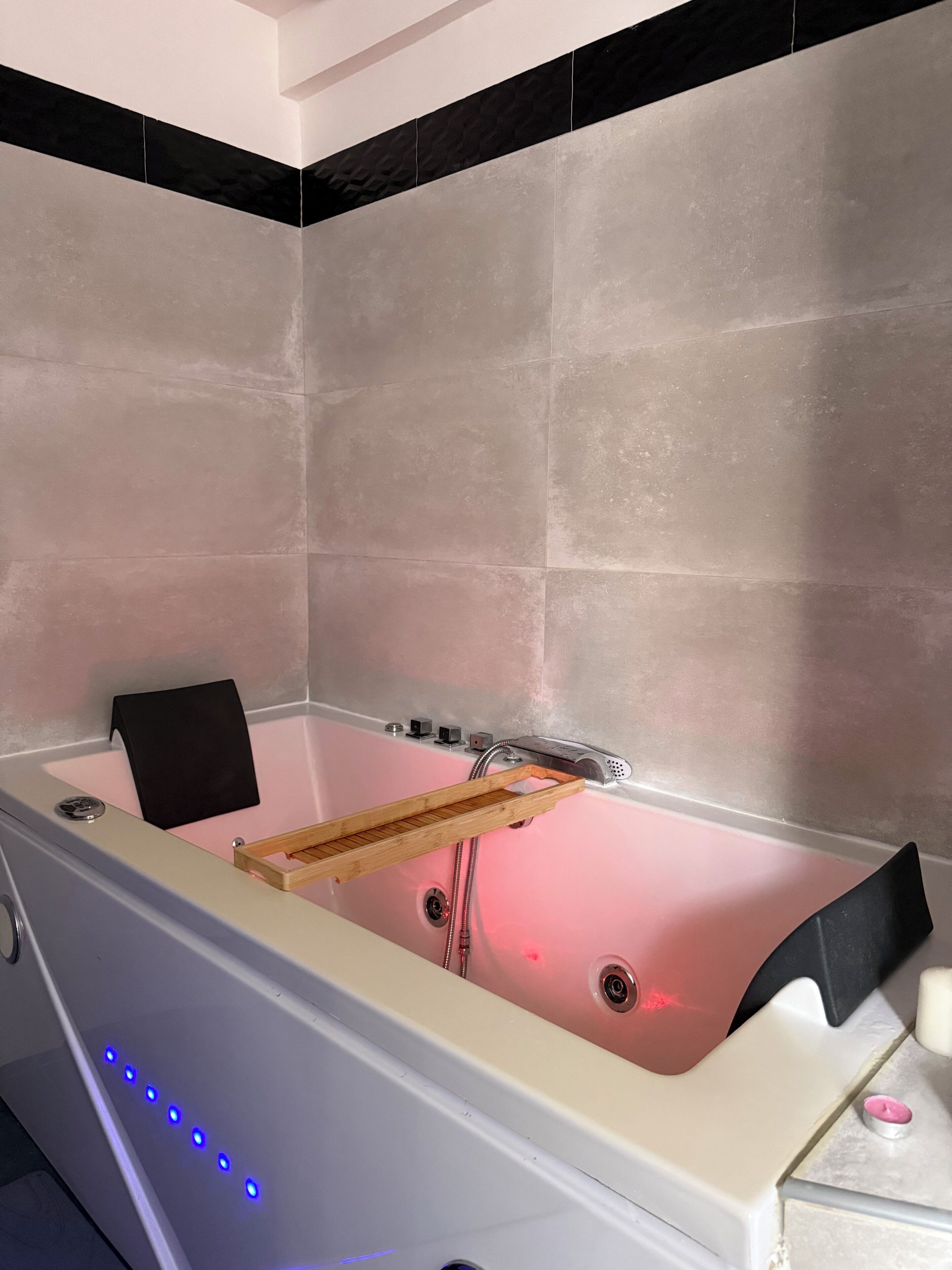 A modern bathroom with a bathtub, a wooden shelf, and LED lights.