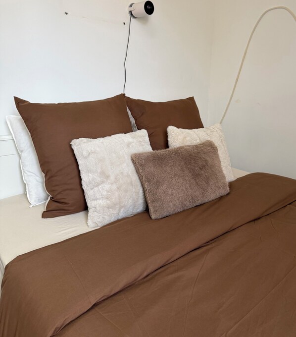 A bed with a brown bedspread and four pillows in various textures and colors.