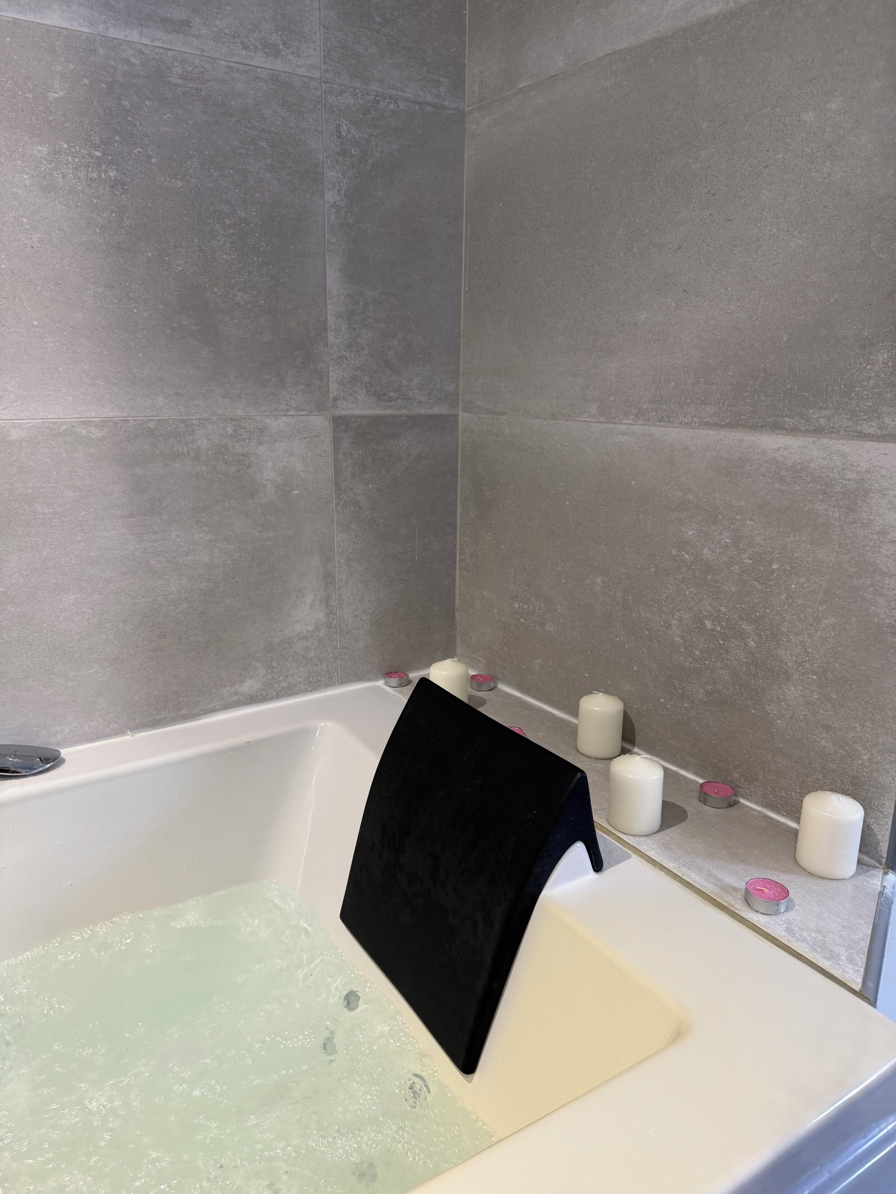 A bathtub with a black towel, a white bath mat, and several candles on a shelf.