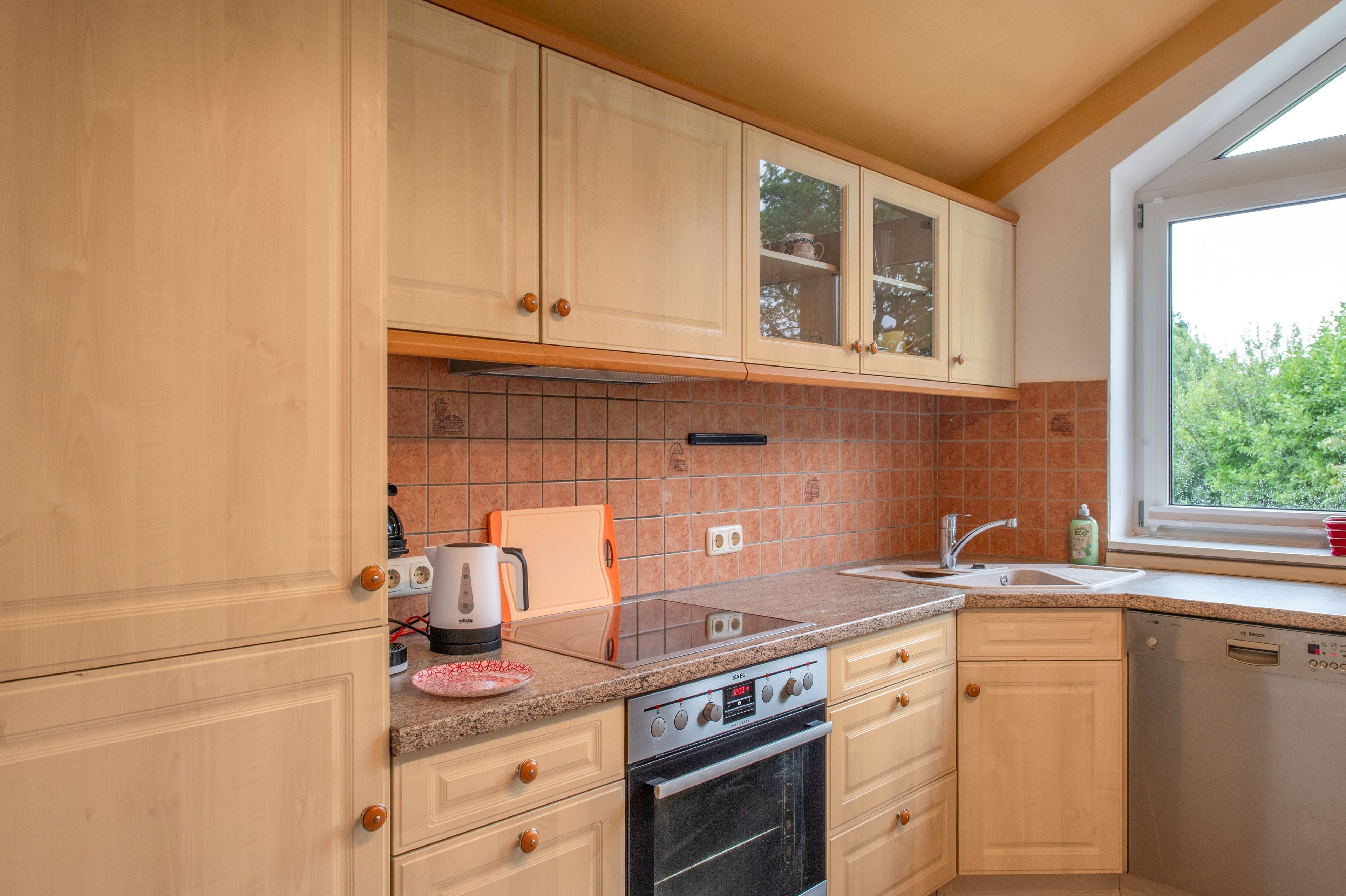 Une cuisine avec des meubles de rangement en bois, une cuisinière, un évier et une fenêtre.