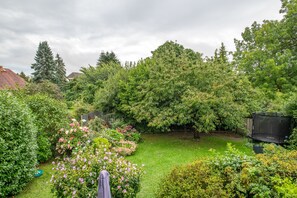 A lush garden with a variety of plants and flowers, a trampoline, and a wooden fence.