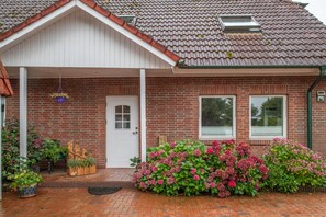 A brick house with a white door, two windows, a small porch, and a brick pathway leading to the entrance.