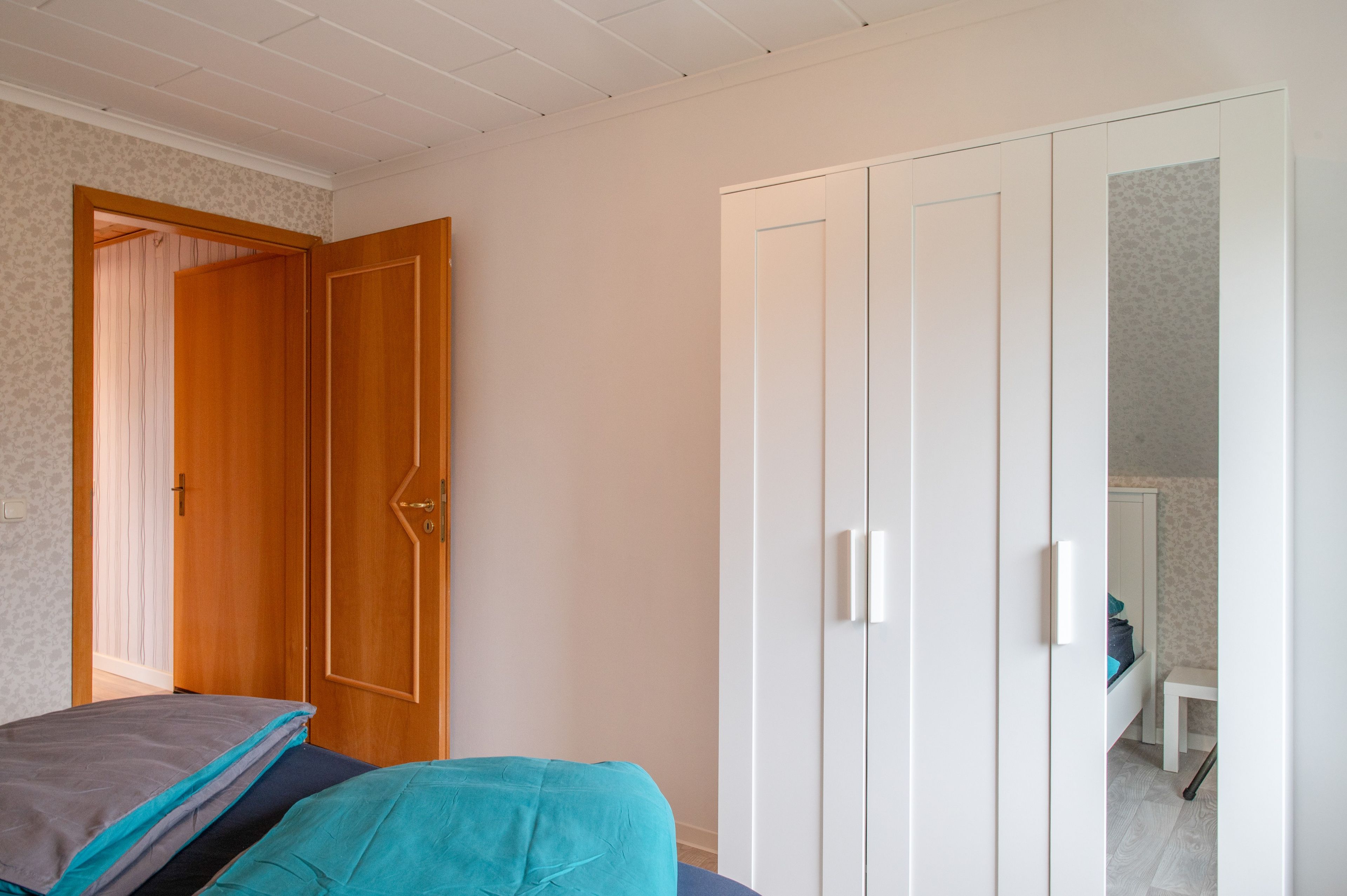 Een slaapkamer met een bed, een kledingkast en een deur naar een andere kamer.