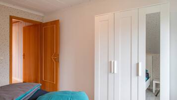 Een slaapkamer met een bed, een kledingkast en een deur naar een andere kamer.