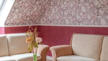 Een kamer met bloemenbehang, een groene vaas met bloemen en twee beige banken.