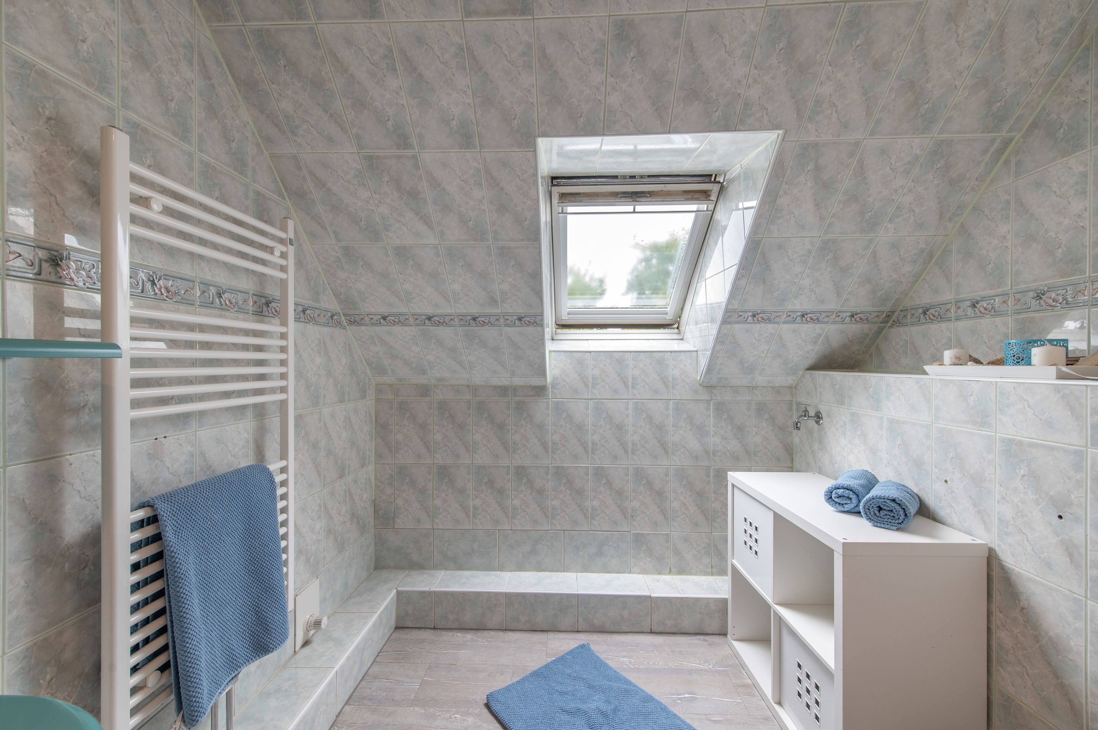 A modern bathroom with a skylight, a bathtub, a shower area, and a white vanity with towels.