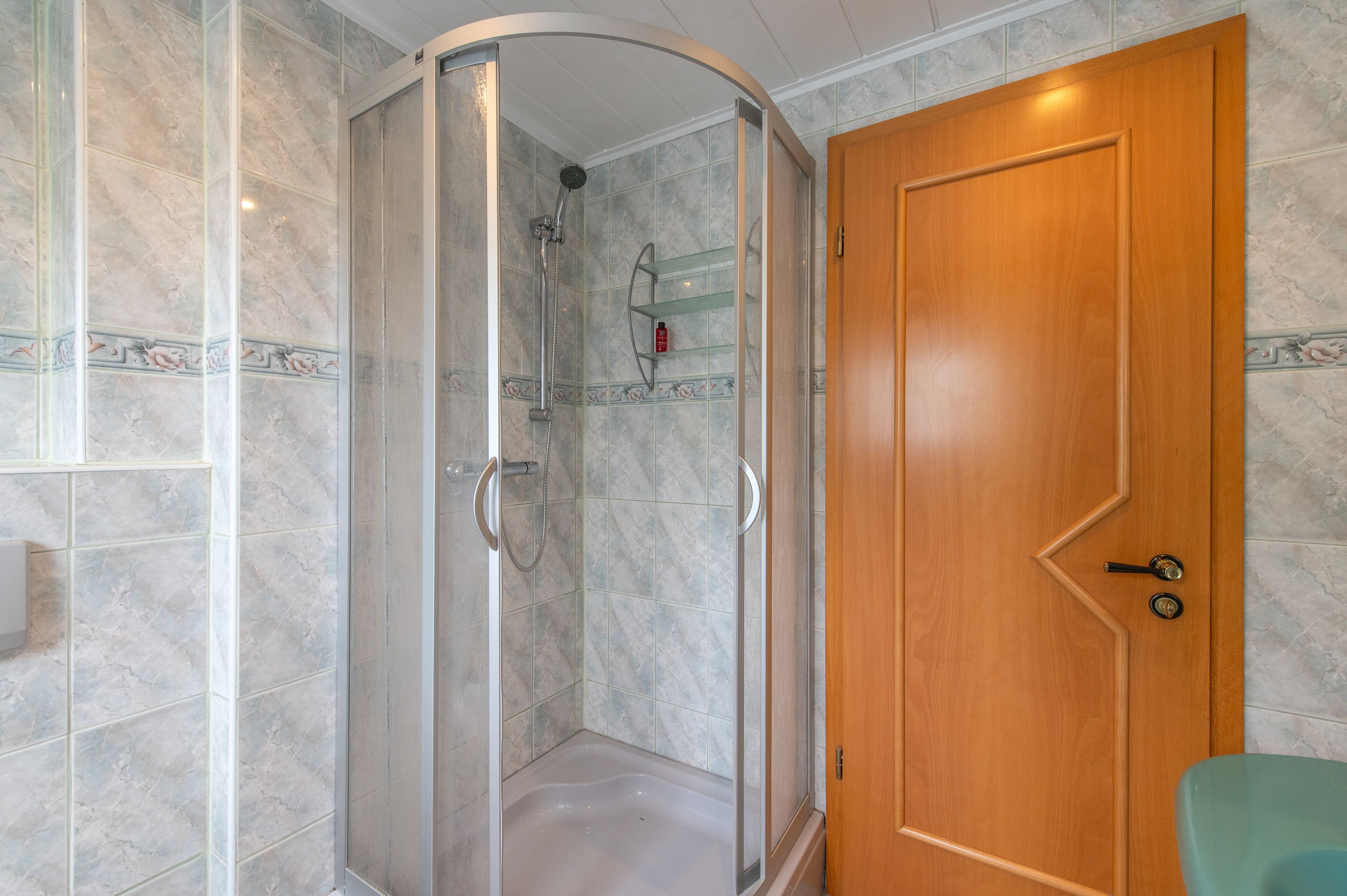 Ein Badezimmer mit einer gläsernen Duschkabine, einer Holztür und Marmorfliesen.