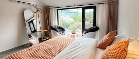 A hotel room with a large bed, a chair, a small table, and a window with a view.