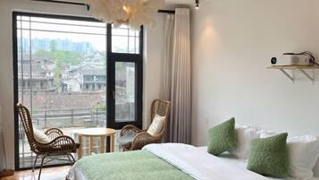A hotel room with a large window, a bed with pillows, a chair, a small table, and a ceiling light fixture.