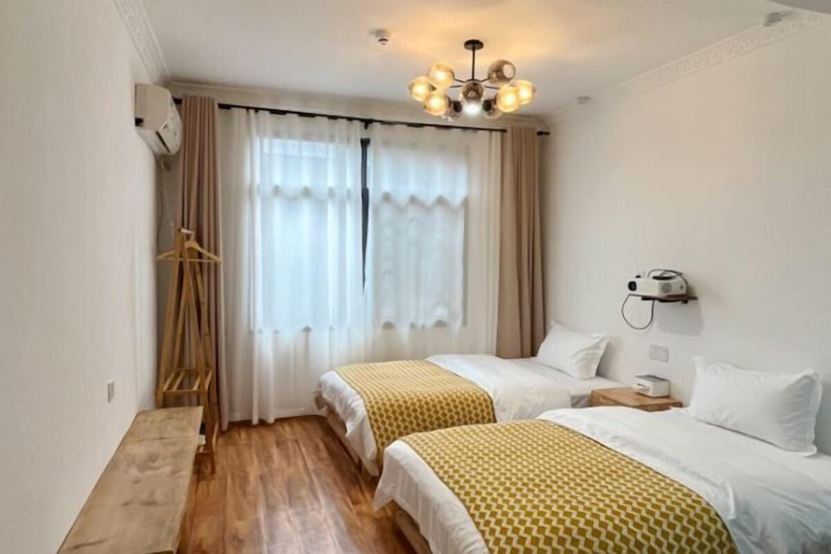 Habitación de hotel con dos camas, piso de madera, escritorio y mesita de noche fijada a la pared.