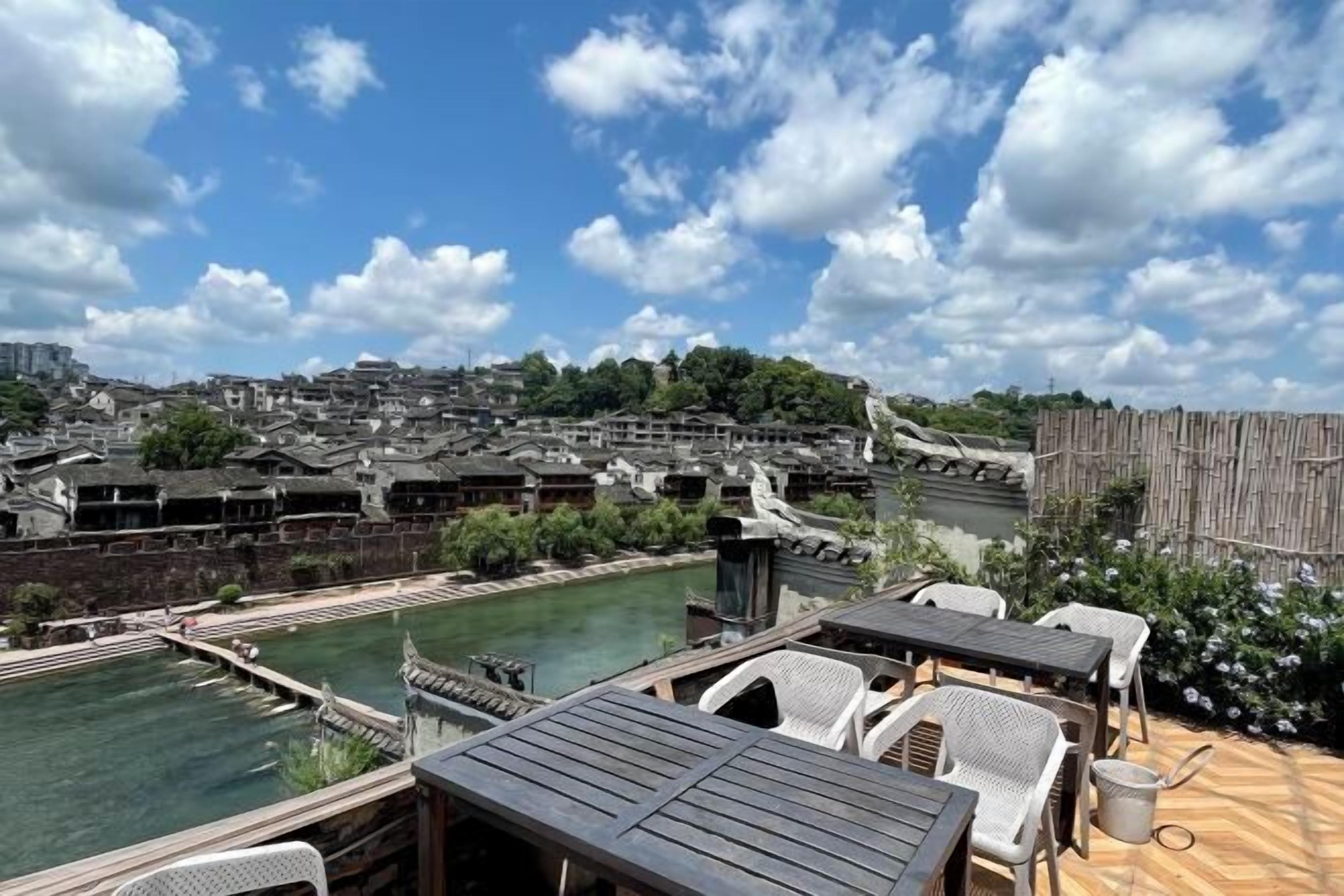A riverside terrace with outdoor seating and a view of traditional buildings.
