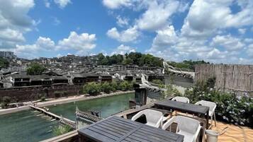 A riverside terrace with outdoor seating and a view of traditional buildings.