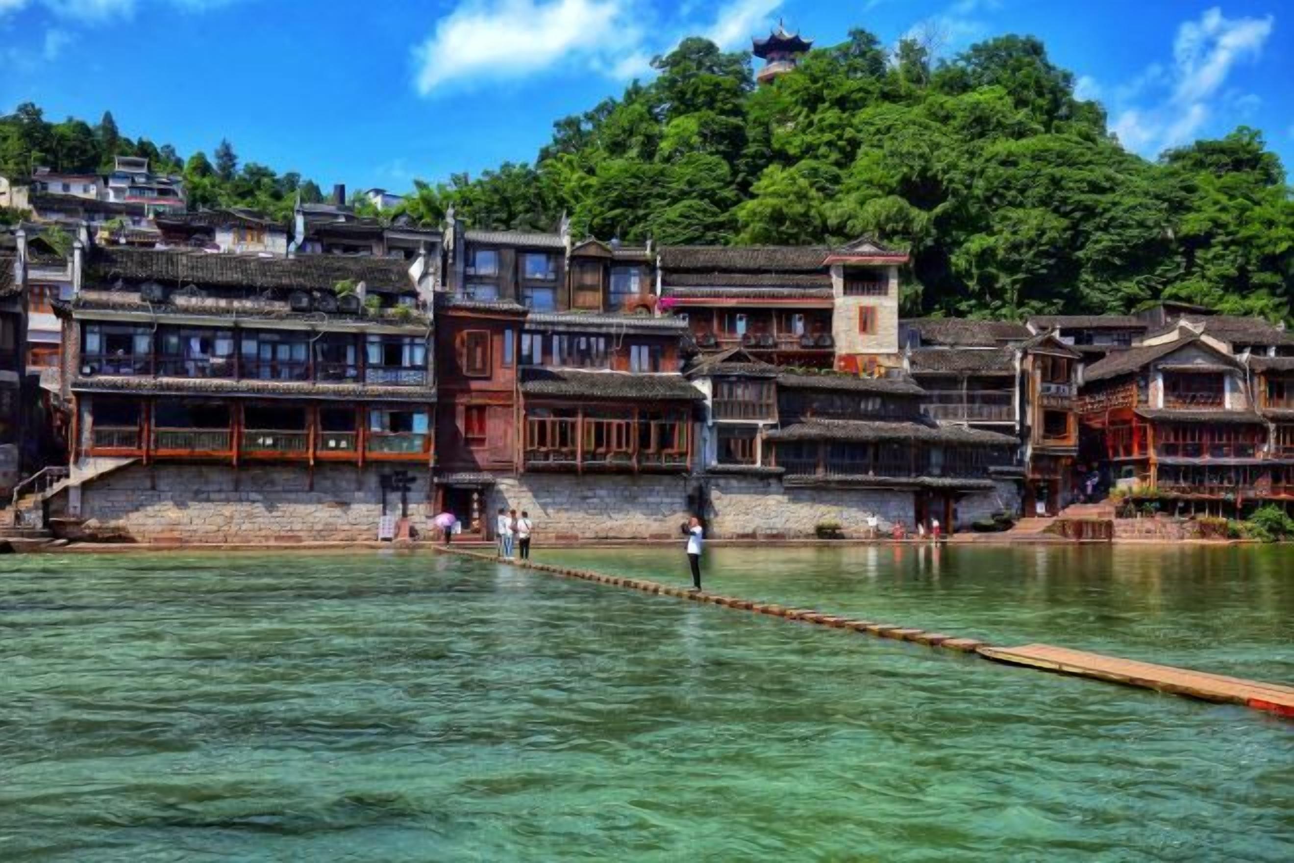 A traditional Chinese water town with tiered buildings along a river, wooden walkways, and clear water.
