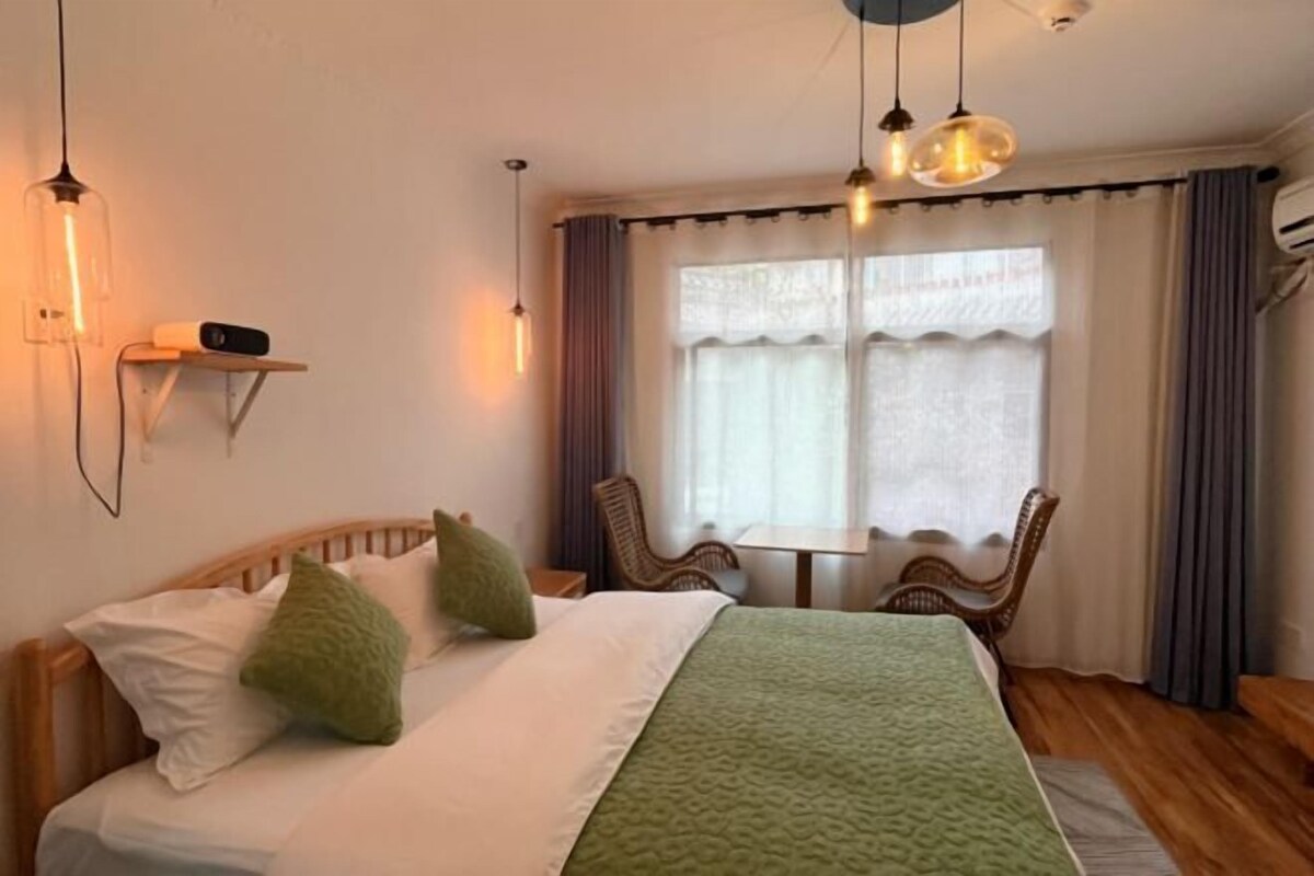 Un dormitorio con cama, mesita de noche, lámpara y ventana con cortinas.