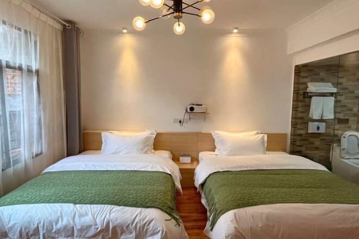Habitación de hotel con dos camas, cabecero de madera, un calefactor en la pared y baño con toallero.